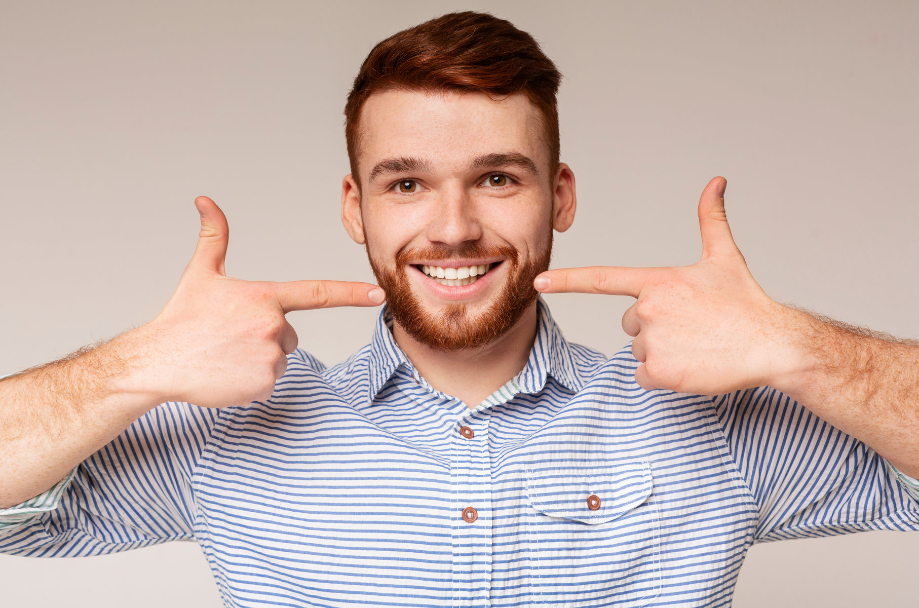 Dental hygiene. Young millennial man showing his beautiful smile and smooth teeth on beige background, panorama